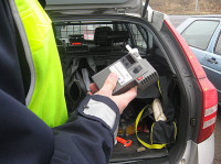Zdjęcie kolorowe, przedstawiające policjanta ruchu drogowego i urządzenie do badania stanu trzeźwości.