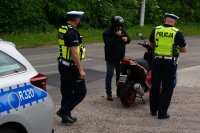 Zdjęcie kolorowe, przedstawiającego policjantów, którzy kontrolują motorowerzystę.