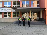 Zdjęcie kolorowe, przedstawiające policjantów i dzieci przed szkołami.