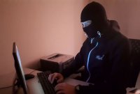 Zdjęcie kolorowe, przedstawiające osobę zamaskowaną przed komputerem.