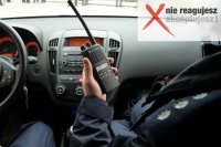 Zdjęcie kolorowe, przedstawiające policjanta w radiowozie, który w ręce trzyma radiotelefon.