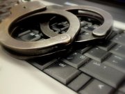 Zdjęcie kolorowe, przedstawiające klawiaturę z komputera i policyjne kajdanki.