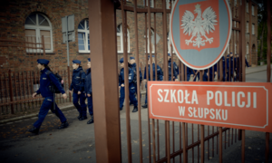 Zdjęcie przedstawiające policjantów maszerujących oraz widoczny napis Szkoła Policji w Słupsku&quot;.