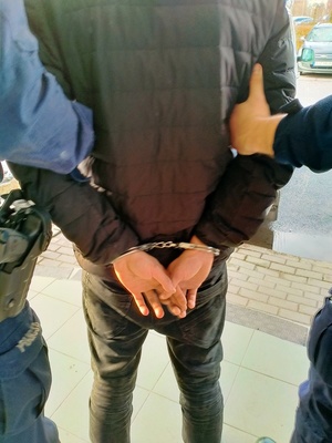 Zdjęcie mężczyzny, który ma założone kajdanki, obok znajduje się policjant.