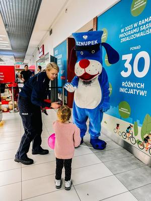 Zdjęcie przedstawiające dziewczynkę witającą sie ze Sznupkiem oraz policjantkę.