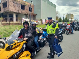 Zdjęcie przedstawiające policjanta oraz pasażera motocyklisty otrzymującą kamizelkę odblaskową.